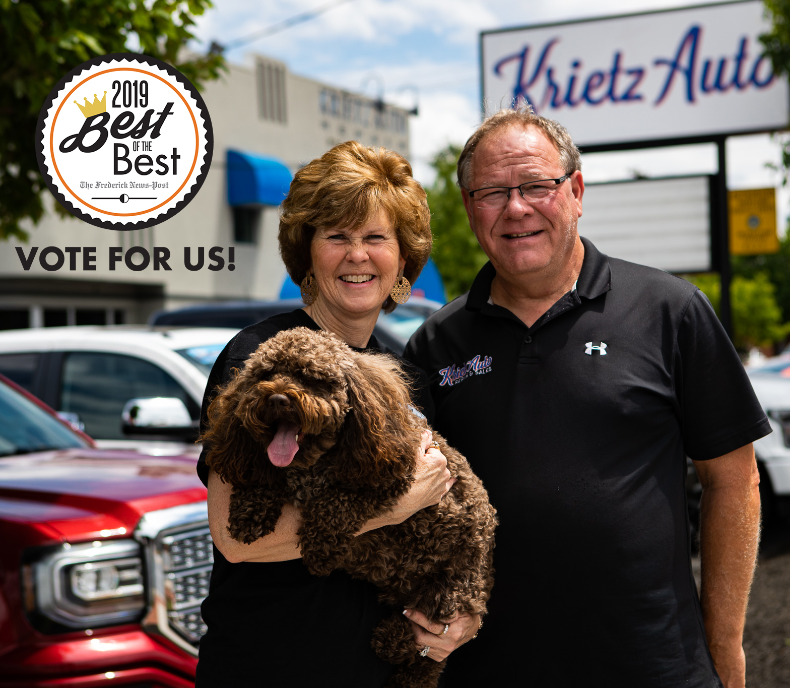 woman and man stand side by side in front of car dealership. woman holds brown dog